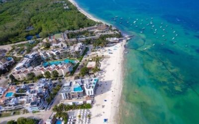 Vue aérienne d'une station balnéaire mexicaine avec des bâtiments modernes bordant une plage de sable blanc et une mer turquoise.