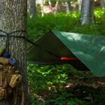Sac à dos fixé à un arbre, hamac sous bâche verte